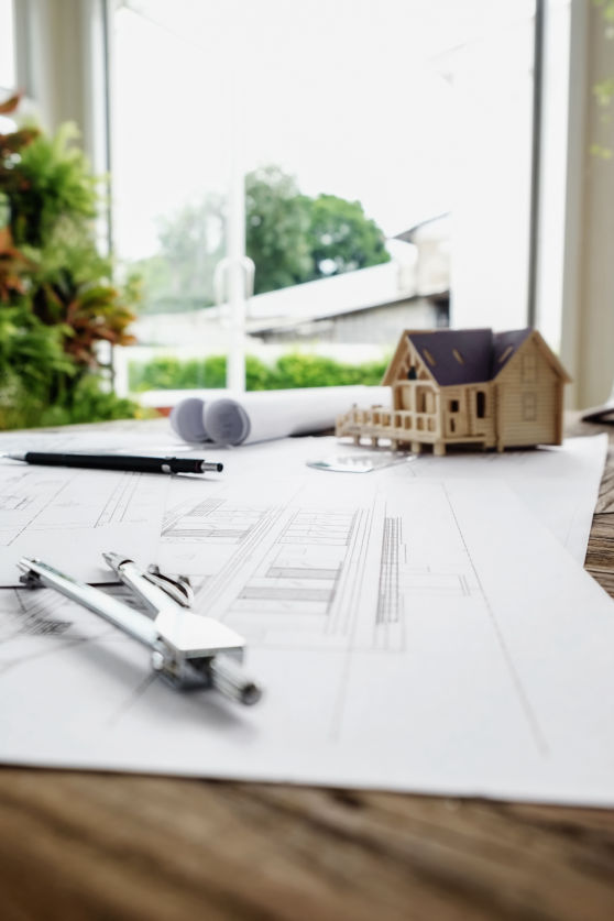 Planos de construcción con compás y maqueta de casa sobre mesa