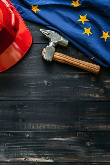 Casco de obra rojo y martillo junto a bandera de la Unión Europea